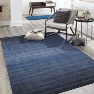 Large rectangular rug featuring a dark blue horizontal gradient on gray wood plank flooring in a bright room.