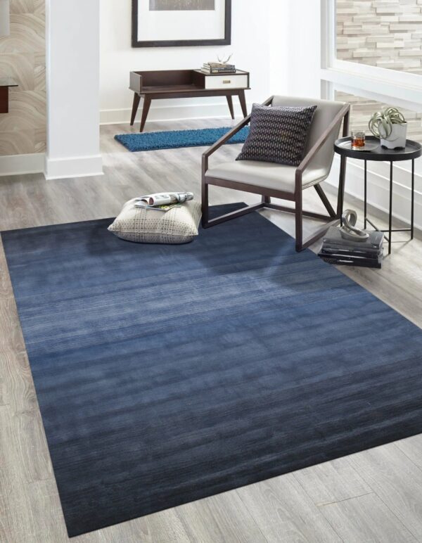 Large rectangular rug featuring a dark blue horizontal gradient on gray wood plank flooring in a bright room.