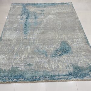Distressed silver and gray rug with blue-green abstract accents rests on glossy light-colored tiles.