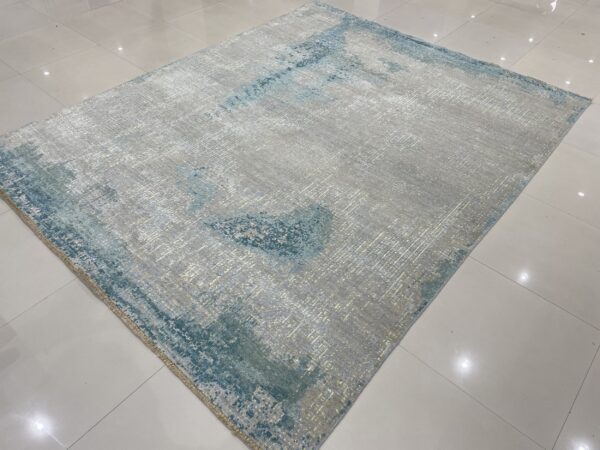 Abstract low pile rug in gray and teal with reflective fiber texture resting on glossy white tile.