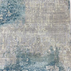 Textured rug displaying abstract blue shapes over a gray field with subtle yellow linear detail and visible fringe.