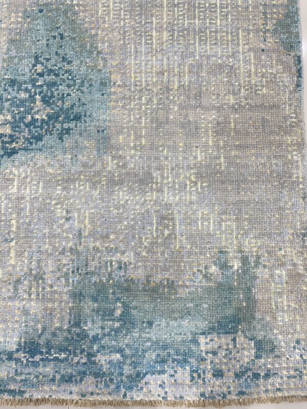 Textured rug displaying abstract blue shapes over a gray field with subtle yellow linear detail and visible fringe.