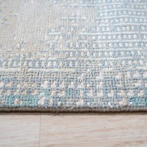 A nubby textured rug in pale blue, cream, and teal sits on light wood planks.