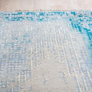 Textured rug with abstract blue, gray, and yellow patterns sitting on light wood flooring.