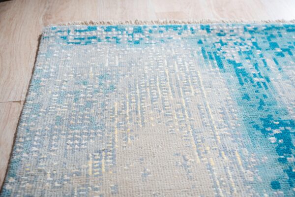 Textured rug with abstract blue, gray, and yellow patterns sitting on light wood flooring.