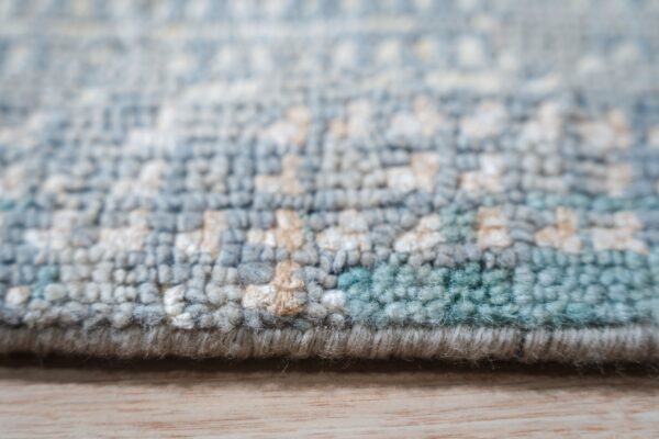 Knotted, medium-pile rug texture in blue, teal, and white abstract patterns on light wood.