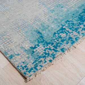 Textured area rug with an abstract design blending gray and bright blue on light wood planks.