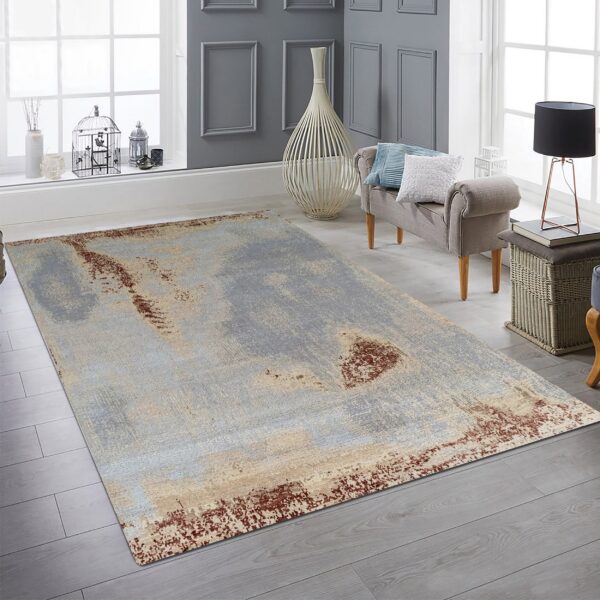 Distressed abstract rug in light blue, tan, and rust colors rests on gray plank flooring in a bright room.