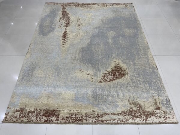Rectangular rug with abstract gray, beige, and rust colors, laid on reflective white square tiles.