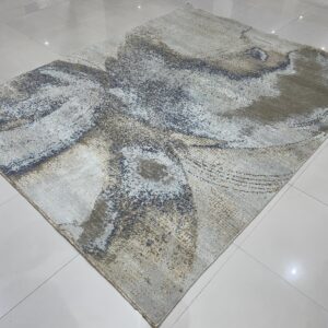 Abstract gray and blue rug with gold highlights displays on a reflective white tile floor.