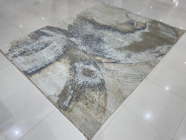 Abstract gray and blue rug with gold highlights displays on a reflective white tile floor.