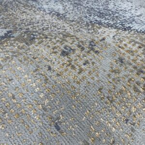 Close-up of a gray textured rug with small, scattered golden pile creating a speckled abstract pattern.