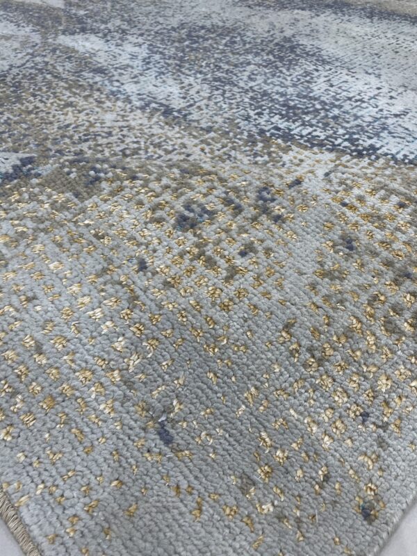 Close-up of a gray textured rug with small, scattered golden pile creating a speckled abstract pattern.