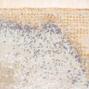 Close-up of a textured rug featuring abstract gray, teal, and gold on a cream background.