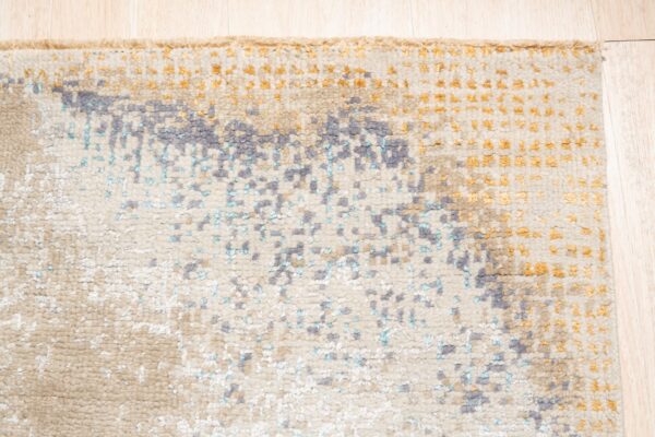 Close-up of a textured rug featuring abstract gray, teal, and gold on a cream background.