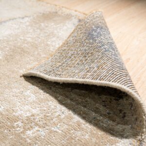 Medium-pile beige rug with abstract pattern folded to show the woven backing on light wood floors.