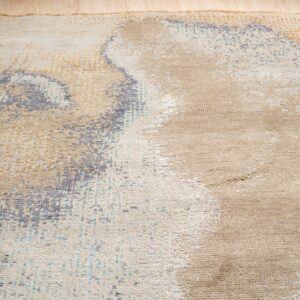 Close-up view of a beige rug featuring an abstract distressed pattern in gold, gray, and light blue.