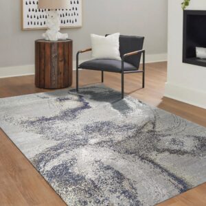 Light gray rug with a distressed blue and silver abstract pattern on medium wood flooring.