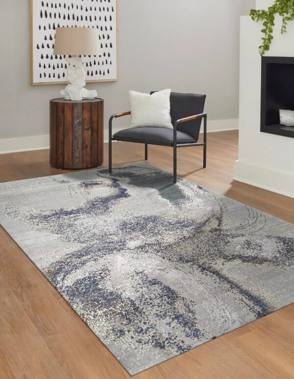 Light gray rug with a distressed blue and silver abstract pattern on medium wood flooring.