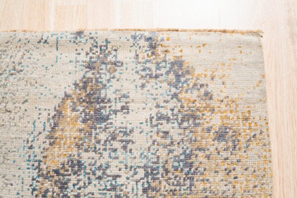 Close-up of a low-pile rug with abstract splotches of gray, blue, and gold on a cream background.