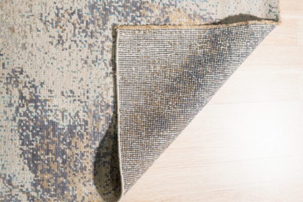 The abstract cream and gray rug is folded back, revealing the woven backing on light wood flooring.