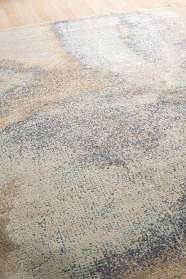 Low-pile rug with abstract distressed patterns in cream, gray, gold, and teal on light wood floors.