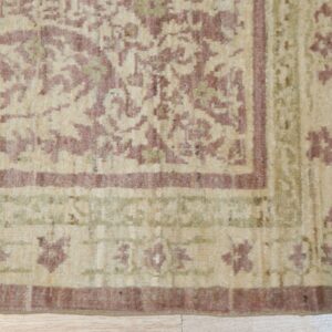 The rug corner displays a dense traditional pattern in soft mauve, cream, and muted green on light wood floor.