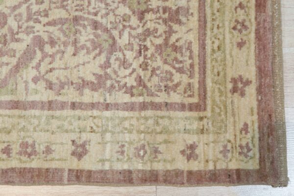 The rug corner displays a dense traditional pattern in soft mauve, cream, and muted green on light wood floor.