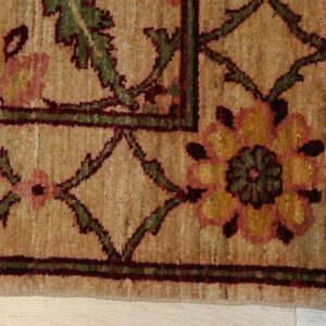 Textured tan rug corner displays a traditional pattern of pink, yellow, green, and dark red motifs on light wood flooring.