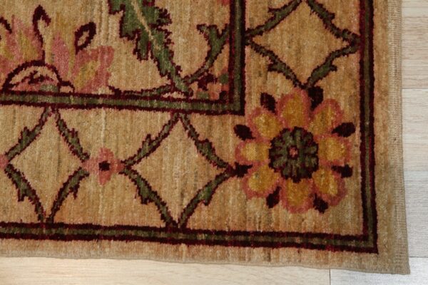 Textured tan rug corner displays a traditional pattern of pink, yellow, green, and dark red motifs on light wood flooring.