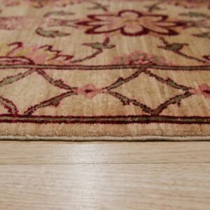 Low angle of a beige floral rug with burgundy and green details, showing the pile edge on wood flooring.