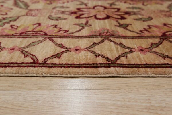 Low angle of a beige floral rug with burgundy and green details, showing the pile edge on wood flooring.