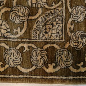 Olive green and tan high-pile rug detail showing a traditional border on pale wood flooring.