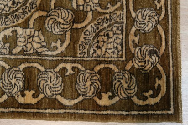 Olive green and tan high-pile rug detail showing a traditional border on pale wood flooring.