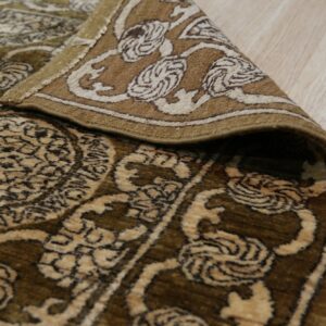 Ornate green and beige traditional rug with medium pile, rolled back on light wood plank flooring.