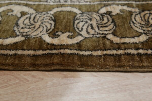 Olive green high-pile rug with beige and dark brown ornate scroll pattern on light wood floor.