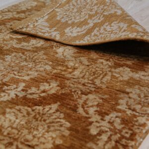 A distressed gold and beige patterned rug is folded over, revealing the backing on light wood flooring.