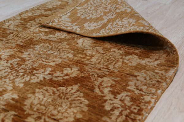 A distressed gold and beige patterned rug is folded over, revealing the backing on light wood flooring.