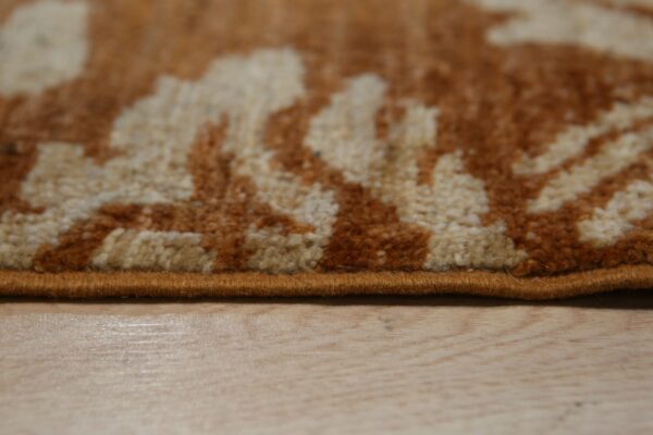 Textured high-pile rug in rust and cream patterns, featuring a bound edge above light wood plank flooring.