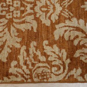 Textured beige and burnt orange rug featuring a scrolling damask pattern on light wood flooring.