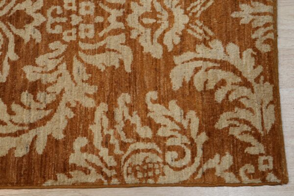 Textured beige and burnt orange rug featuring a scrolling damask pattern on light wood flooring.