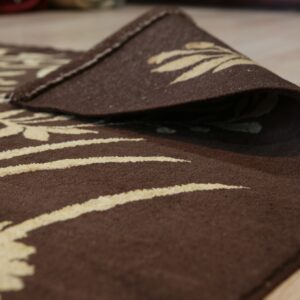 A brown floral rug with light beige details is curled up on a light wood floor.