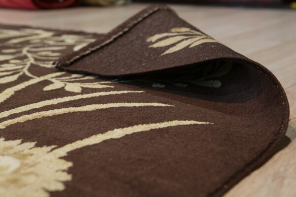 A brown floral rug with light beige details is curled up on a light wood floor.