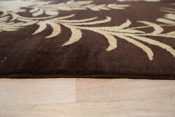 Medium pile brown rug with beige scrolling designs rests on light plank flooring.