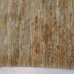 Thick, shaggy rug surface with vertical bands of gold, cream, and brown resting on light wood floor.