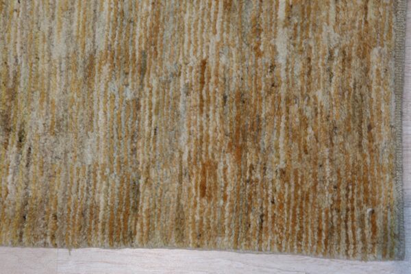 Thick, shaggy rug surface with vertical bands of gold, cream, and brown resting on light wood floor.