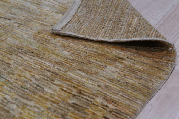 Multicolored striped rug in beige and gold is folded back, revealing its tightly woven backing on light wood.