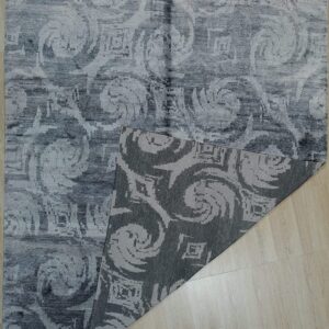 Abstract gray rug with swirling, low pile pattern displayed on light wood flooring.