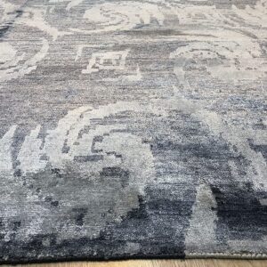 A gray and white rug with a highly distressed scrolling pattern rests on light wood flooring.