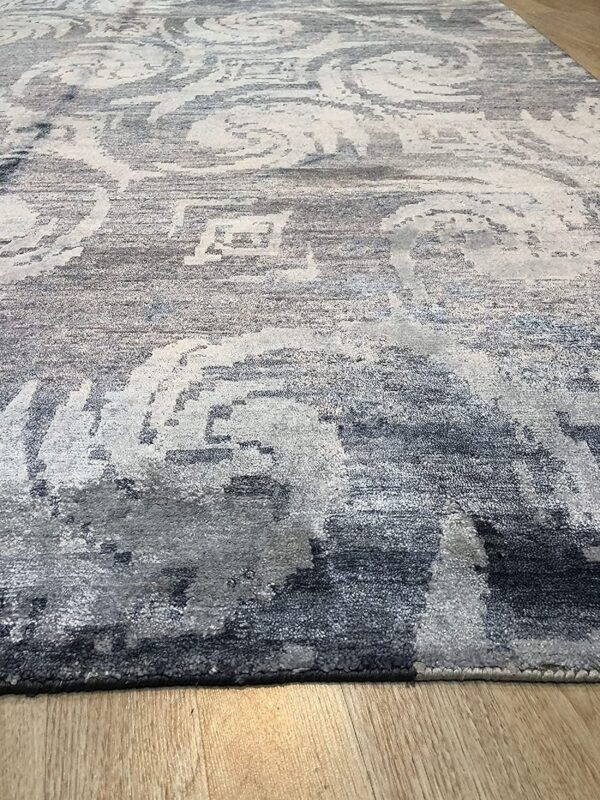 A gray and white rug with a highly distressed scrolling pattern rests on light wood flooring.